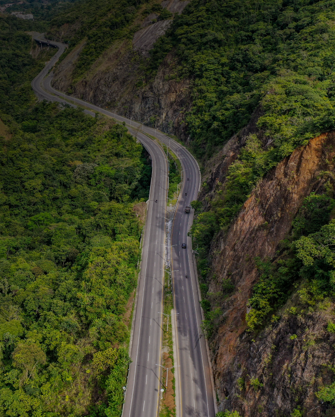 Aerial view of a winding road cutting through a lush green mountainous landscape